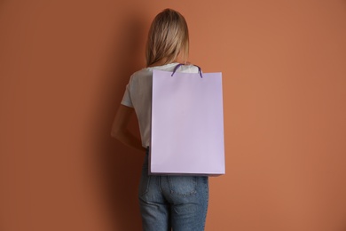 Photo of Woman with paper shopping bag on light brown background, back view