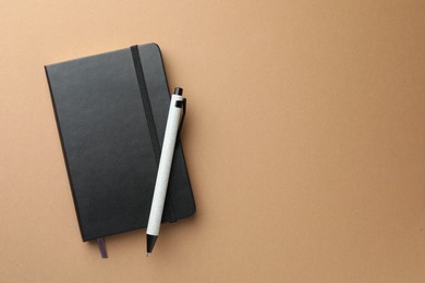 Closed black notebook and pen on light brown background, top view. Space for text