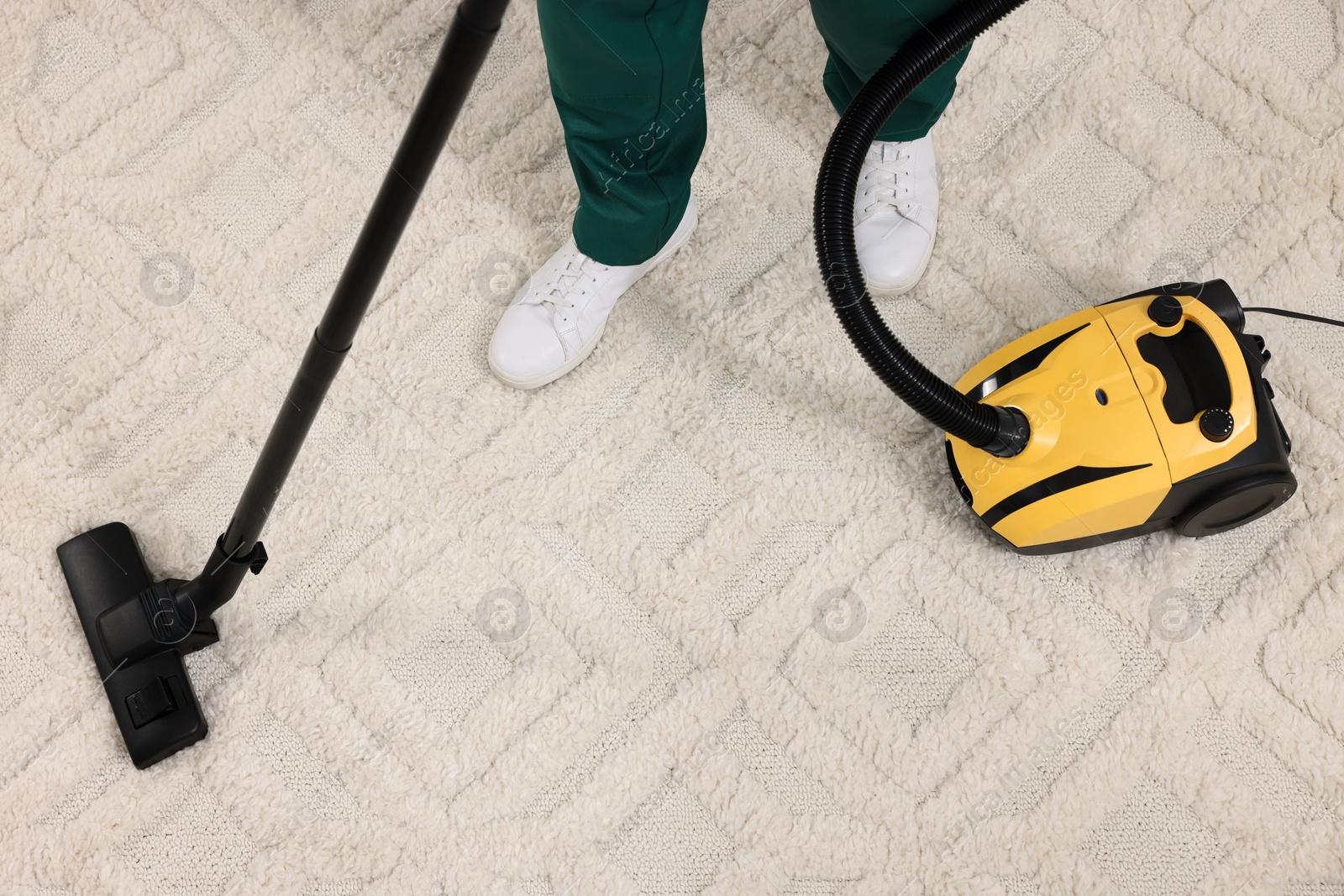 Photo of Dry cleaner's employee hoovering carpet with vacuum cleaner, above view