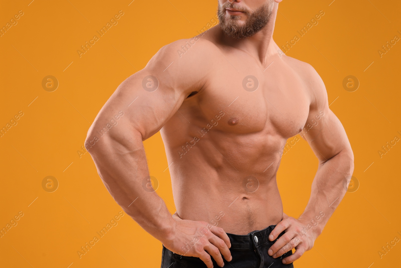Photo of Muscular man showing abs on orange background, closeup. Sexy body