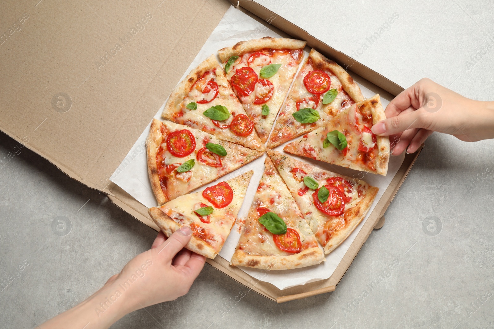 Photo of People taking slices of delicious pizza Margherita from box at light grey table, top view