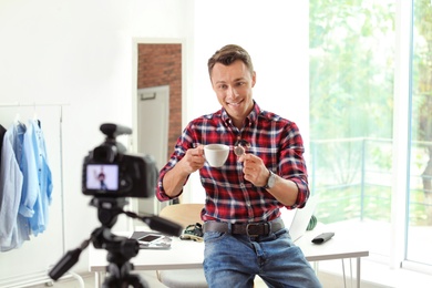 Photo of Fashion blogger with cup of coffee and wristwatch recording video on camera at home