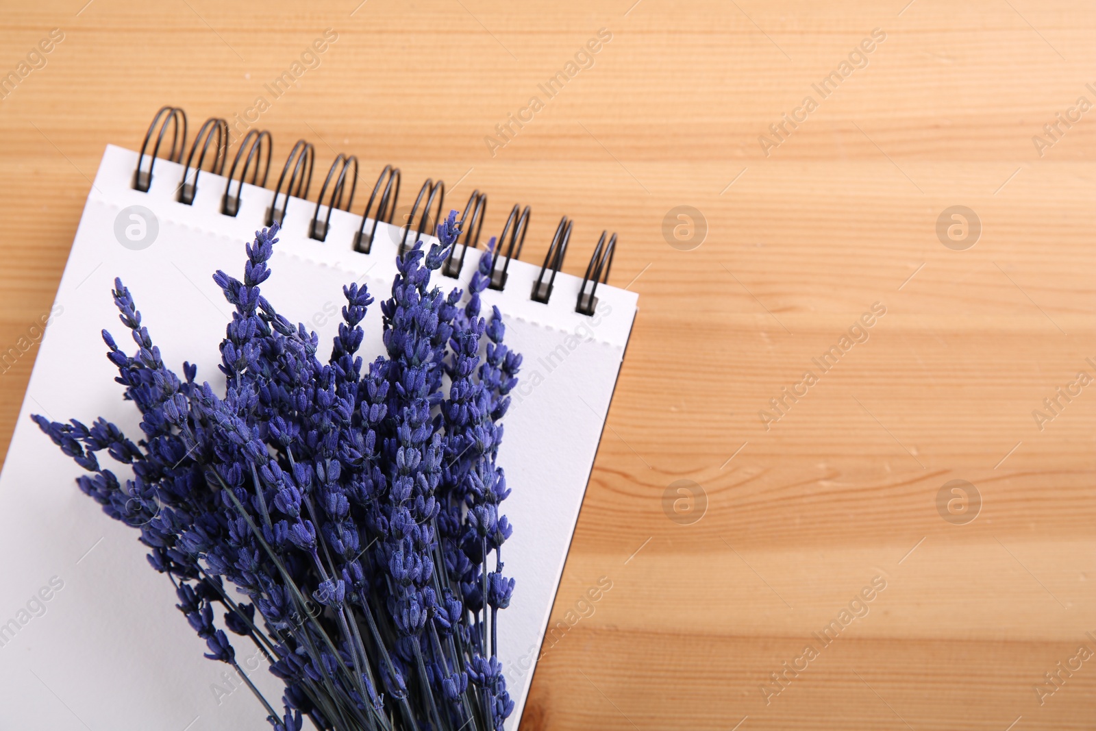 Photo of Bouquet of beautiful preserved lavender flowers and notebook on wooden table, top view. Space for text