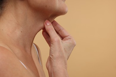 Photo of Mature woman touching her neck on beige background, closeup. Space for text