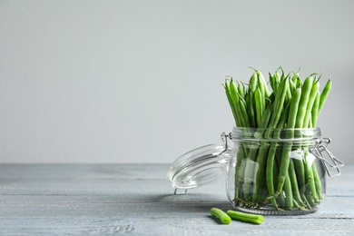 Photo of Fresh green beans in glass jar on grey wooden table, space for text