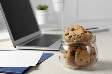 Photo of Jar with chocolate chip cookies on white wooden table in office, closeup. Space for text
