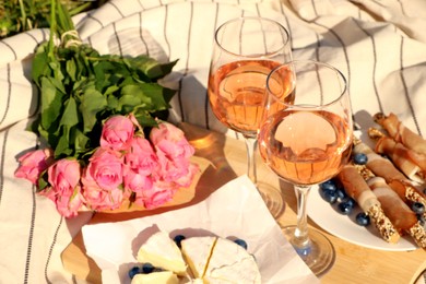 Glasses of delicious rose wine, flowers and food on picnic blanket outdoors