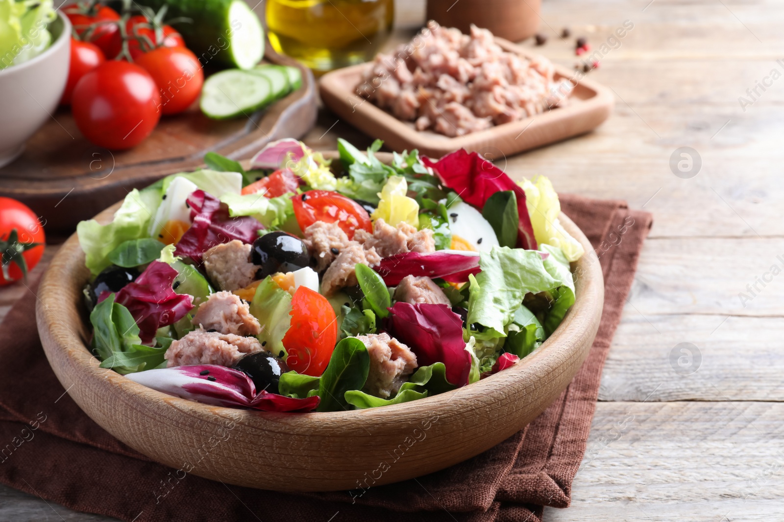 Photo of Bowl of delicious salad with canned tuna and vegetables on wooden table