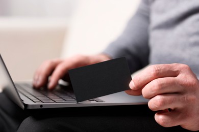 Photo of Man with laptop holding blank business card on blurred background, closeup