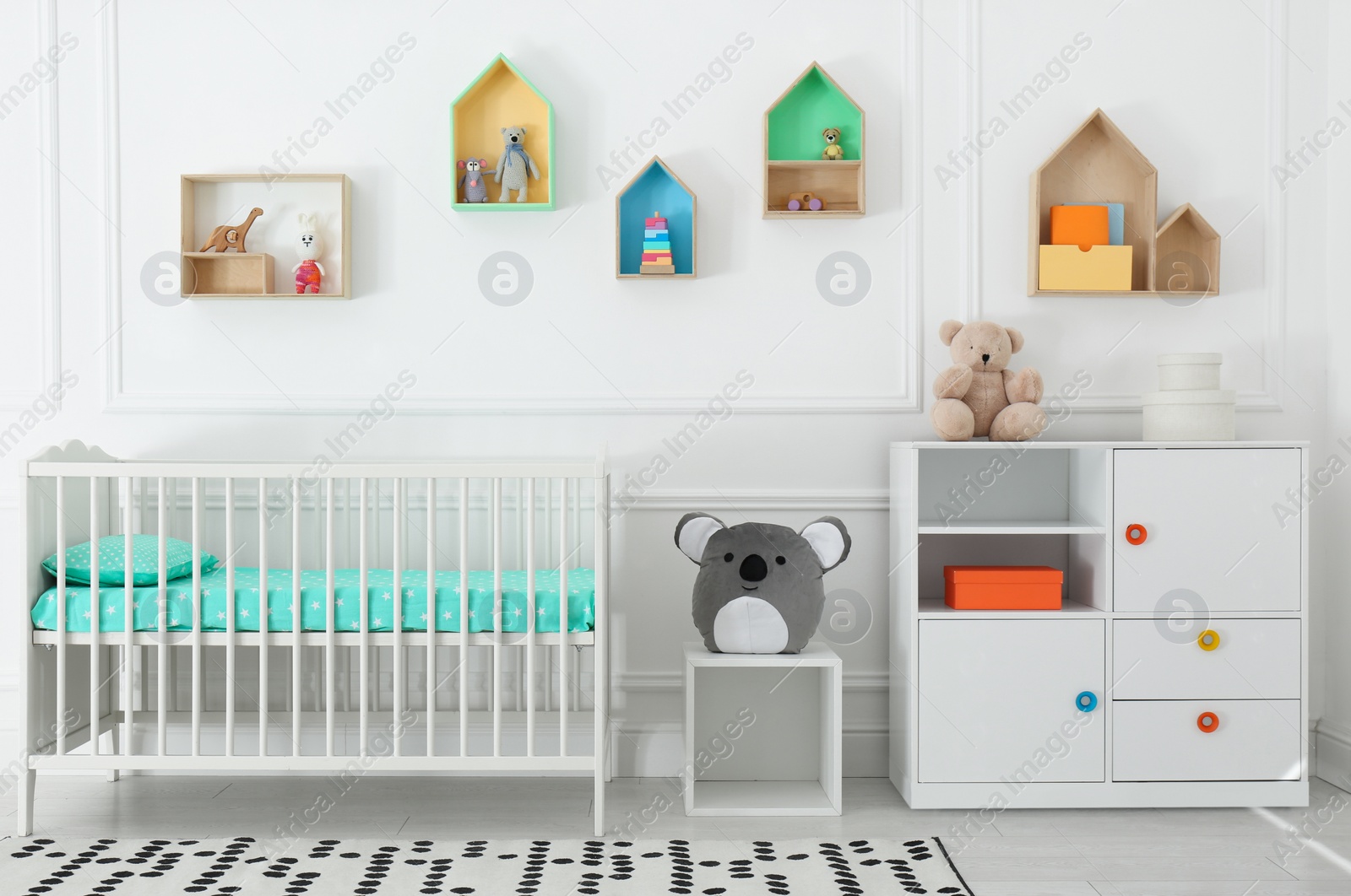 Photo of Comfortable crib near wall with color shelves in baby room. Interior design