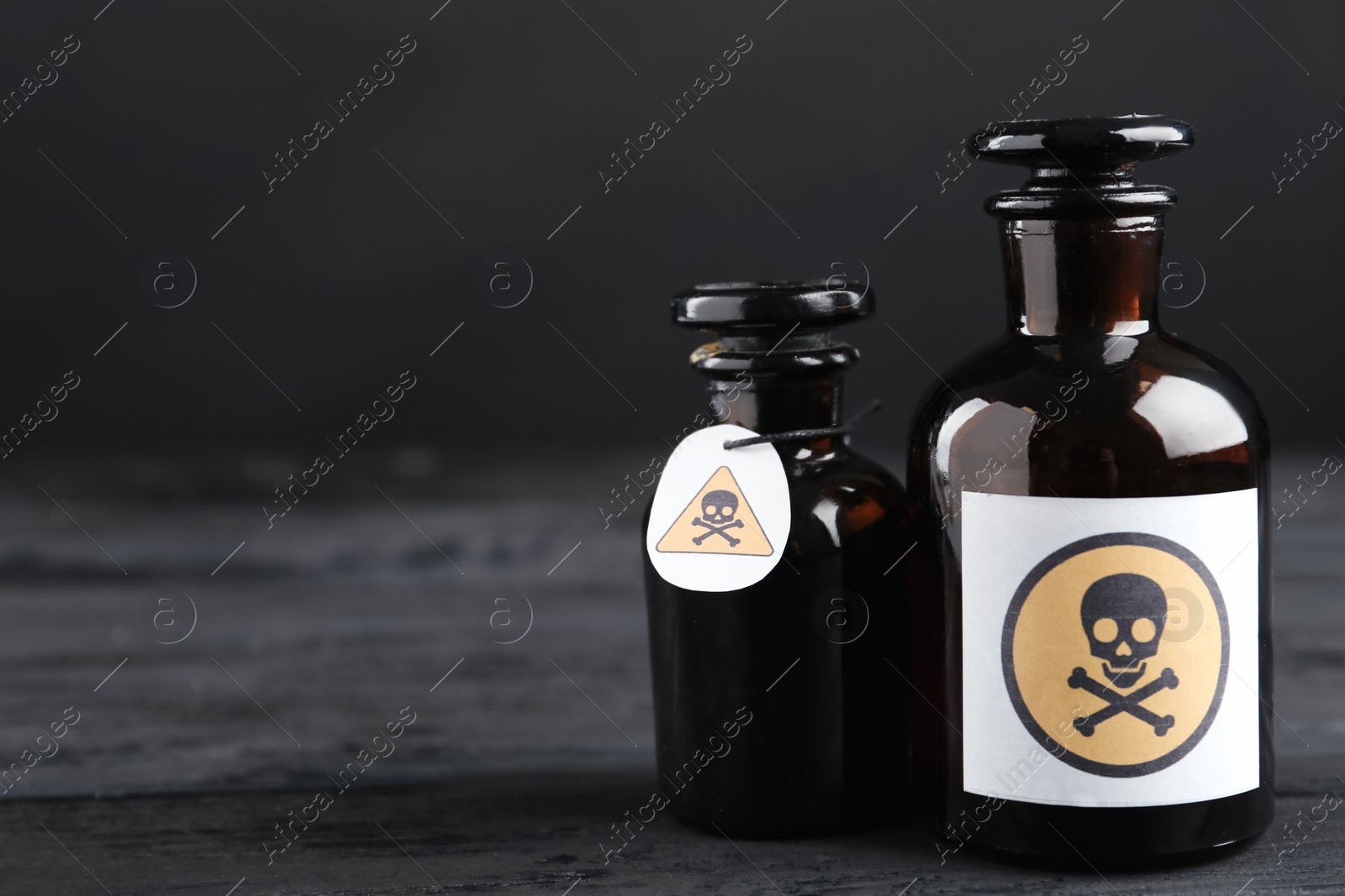 Photo of Glass bottles of poison with warning signs on black wooden table. Space for text