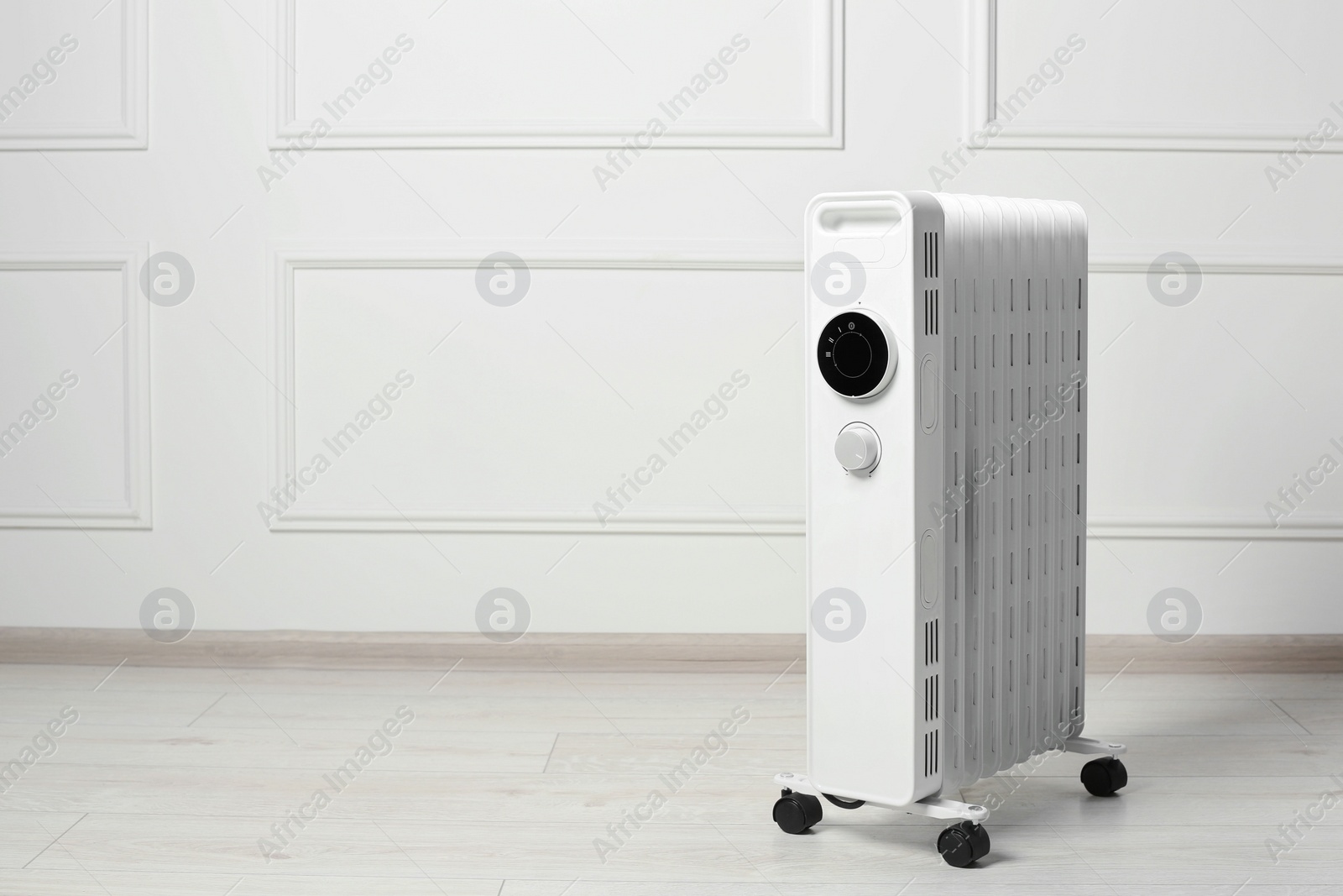 Photo of Modern portable electric heater on floor near white wall indoors, space for text