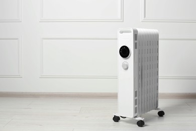 Photo of Modern portable electric heater on floor near white wall indoors, space for text