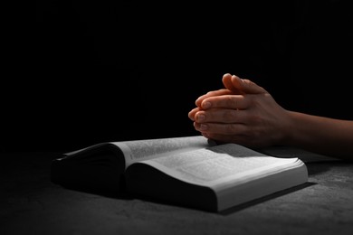Photo of Religion. Christian woman praying over Bible at table against black background, closeup. Space for text