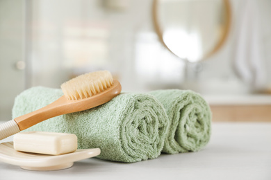 Photo of Clean rolled towels, massage brush and bar of soap on table in bathroom