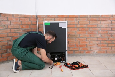 Photo of Male technician in uniform repairing refrigerator indoors. Space for text