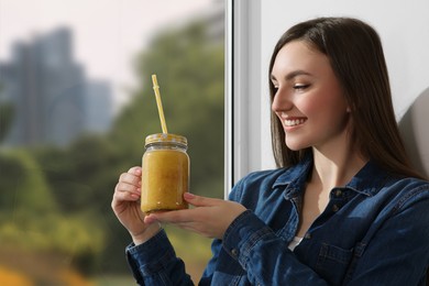 Photo of Beautiful young woman with delicious smoothie near window