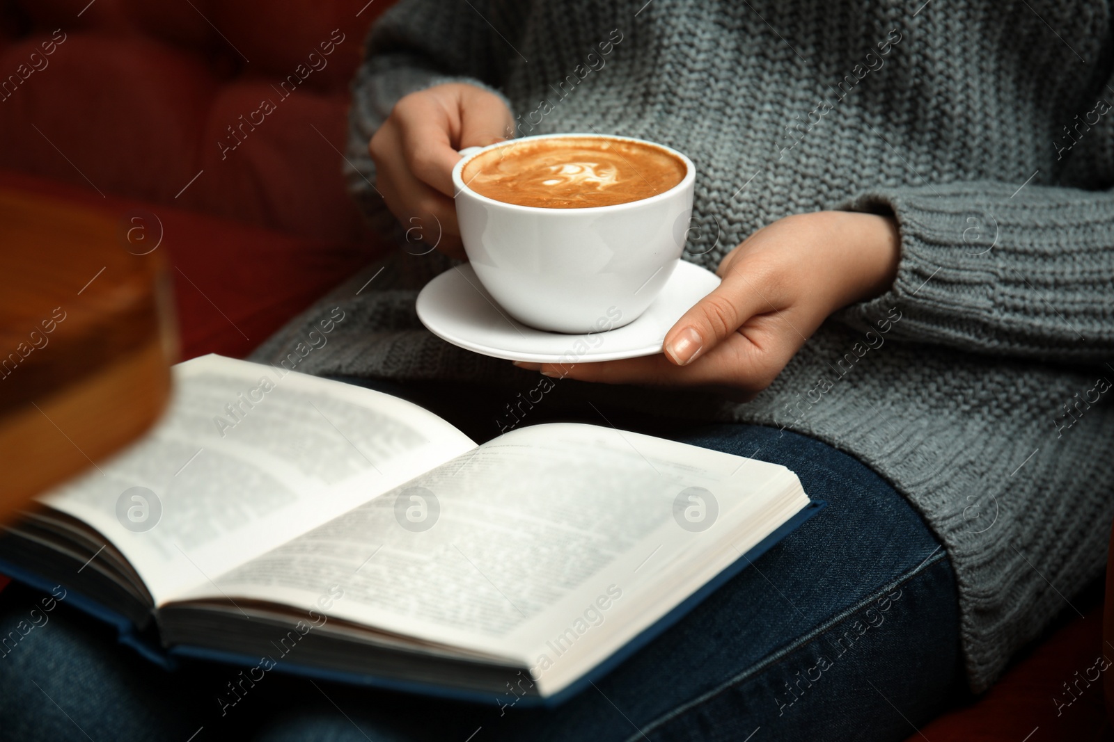 Photo of Woman with cup of coffee reading book on sofa, closeup