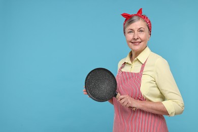 Photo of Happy housewife with frying pan on light blue background, space for text