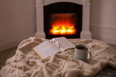 Cup of hot tea and book near fireplace at home. Cozy atmosphere