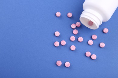 Photo of Bottle and vitamin pills on blue background, above view. Space for text