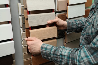 Man choosing wooden flooring among different samples in shop, closeup