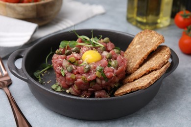 Photo of Tasty beef steak tartare served with yolk, capers and bread on light grey table