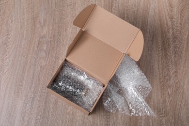 Photo of Jar in cardboard box and bubble wrap on wooden table, top view