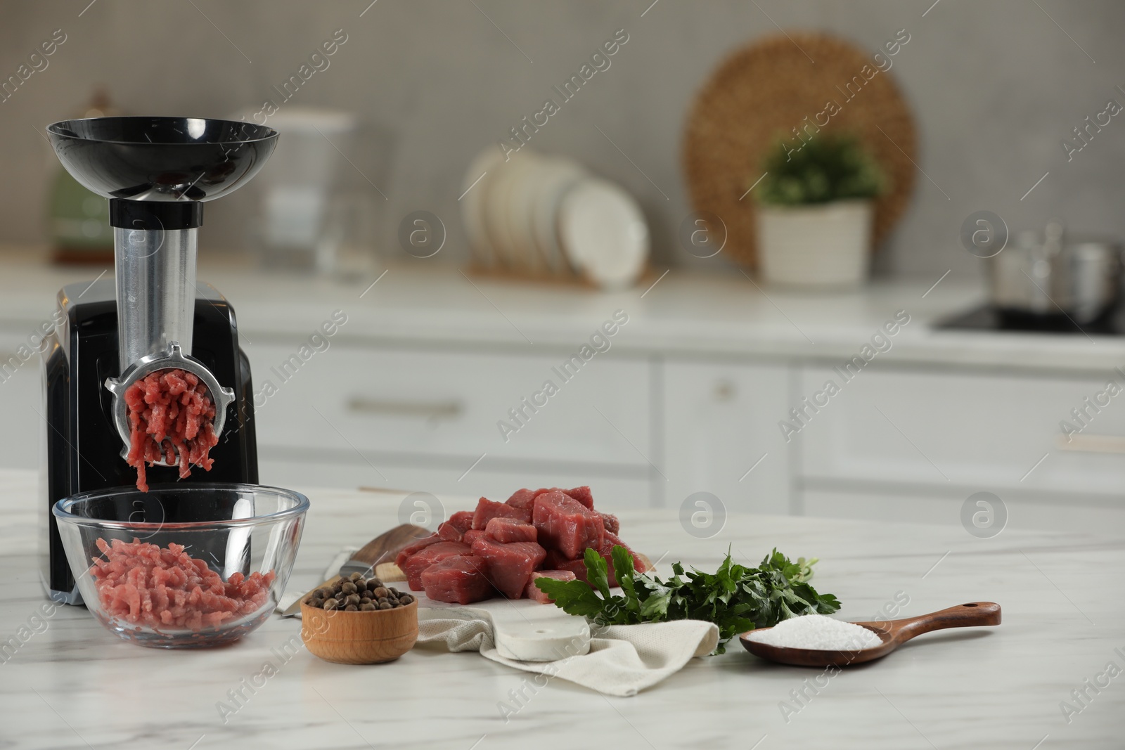 Photo of Electric meat grinder with beef mince, parsley, salt and peppercorns on white table in kitchen