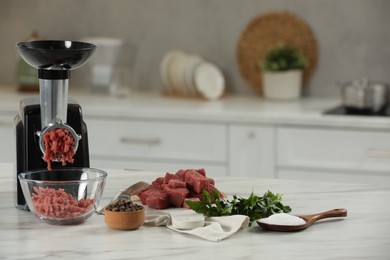 Electric meat grinder with beef mince, parsley, salt and peppercorns on white table in kitchen