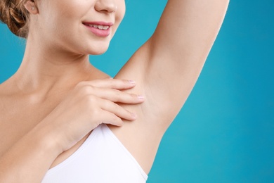 Photo of Young woman with smooth clean armpit on teal background, closeup. Using deodorant