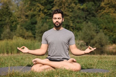 Photo of Man practicing yoga on mat outdoors. Lotus pose