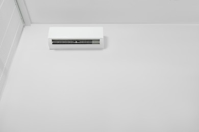 Modern air conditioner on white wall indoors, low angle view. Space for text