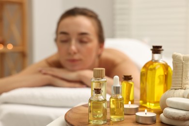 Photo of Aromatherapy. Woman relaxing on massage couch in spa salon, focus on bottles of essential oils, herbal bag, burning candle and stones