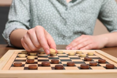 Photo of Playing checkers. Woman thinking about next move at wooden table, closeup