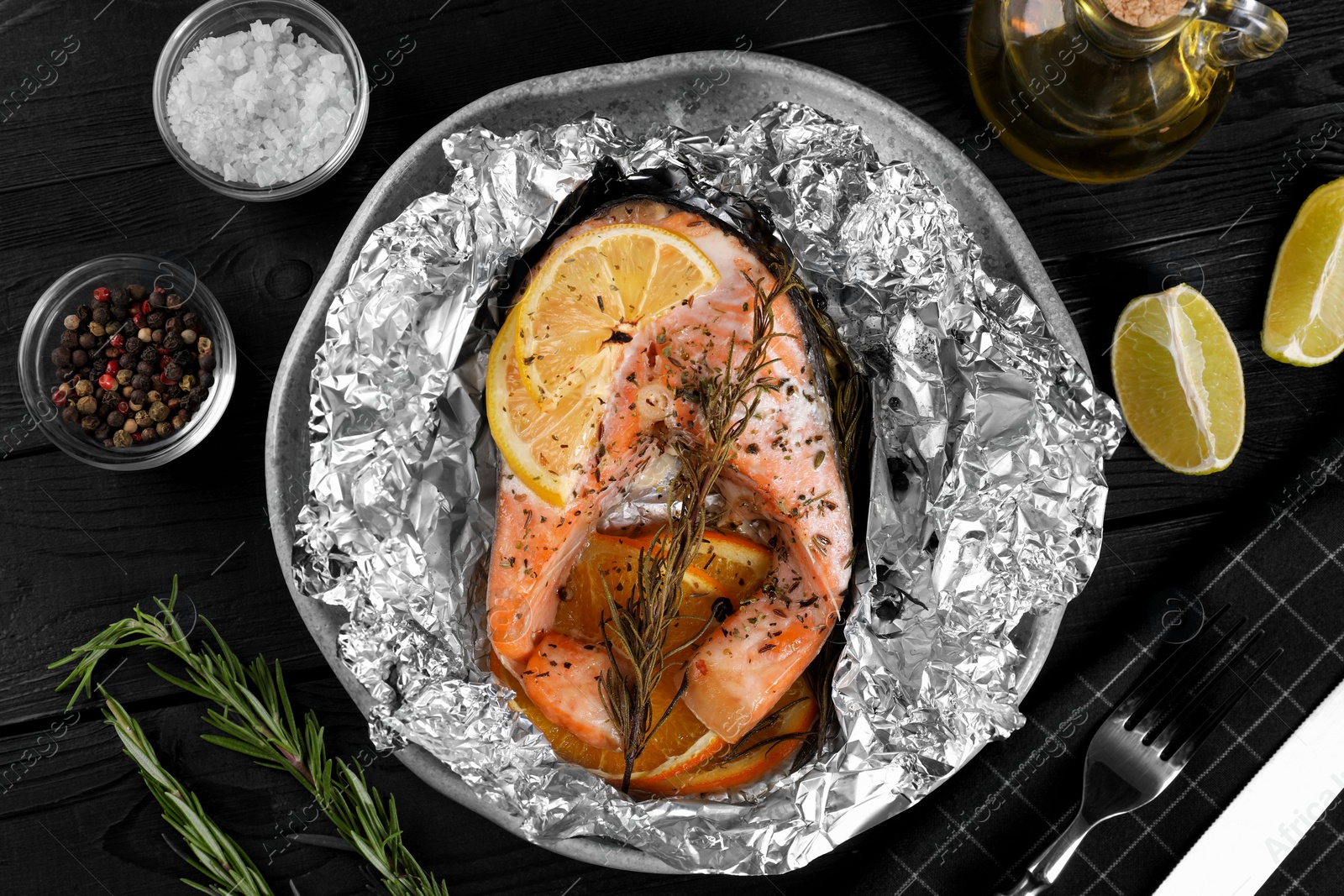 Photo of Tasty salmon baked in foil with lemon, spices and rosemary served on dark wooden table, flat lay