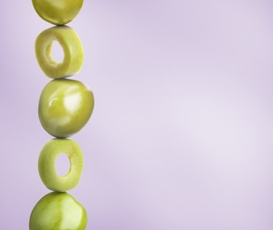 Cut and whole green olives on light violet gradient background, space for text