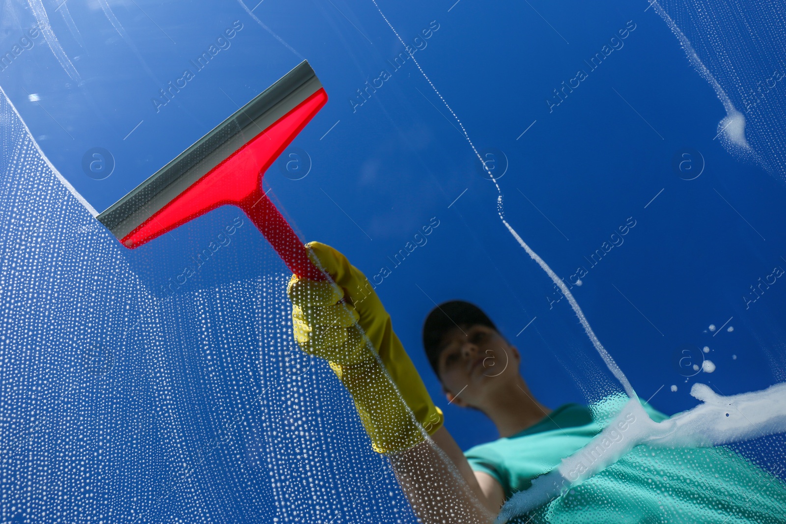 Photo of Woman cleaning glass with squeegee on sunny day