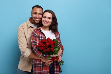 Photo of Happy couple celebrating Valentine's day. Beloved woman with bouquet of red roses on light blue background. Space for text