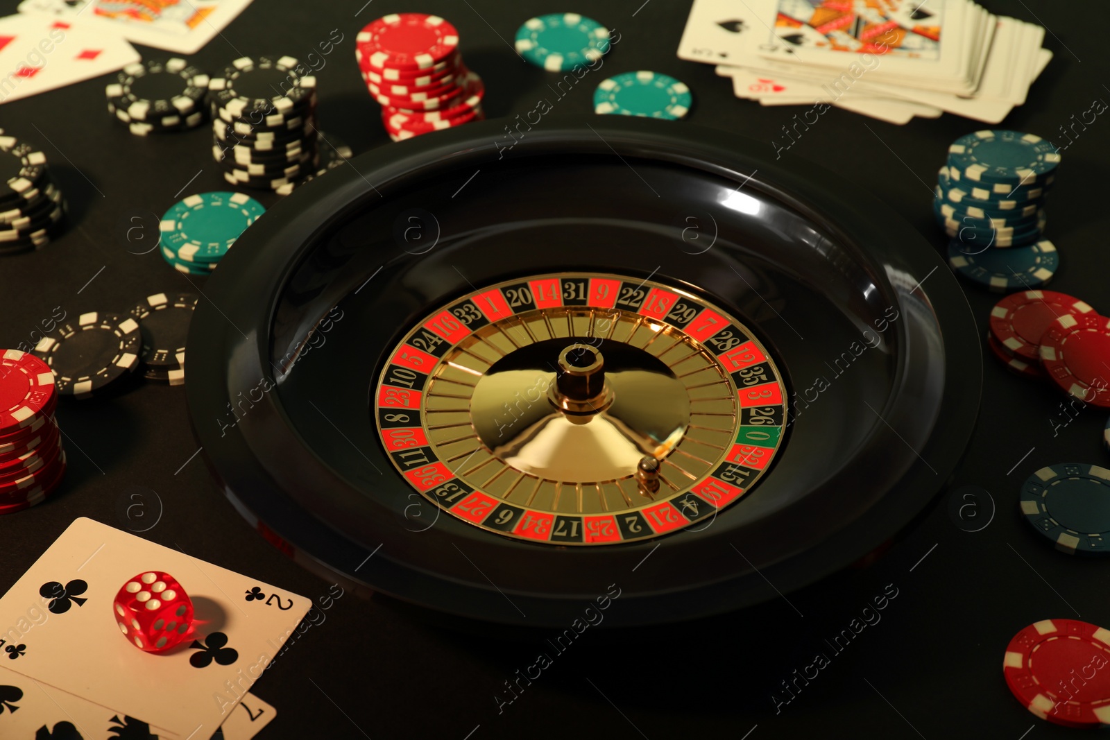 Photo of Roulette wheel, playing cards and chips on table, closeup. Casino game