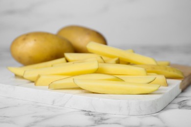 Photo of Whole and cut raw potatoes on white marble table, closeup. Cooking delicious French fries