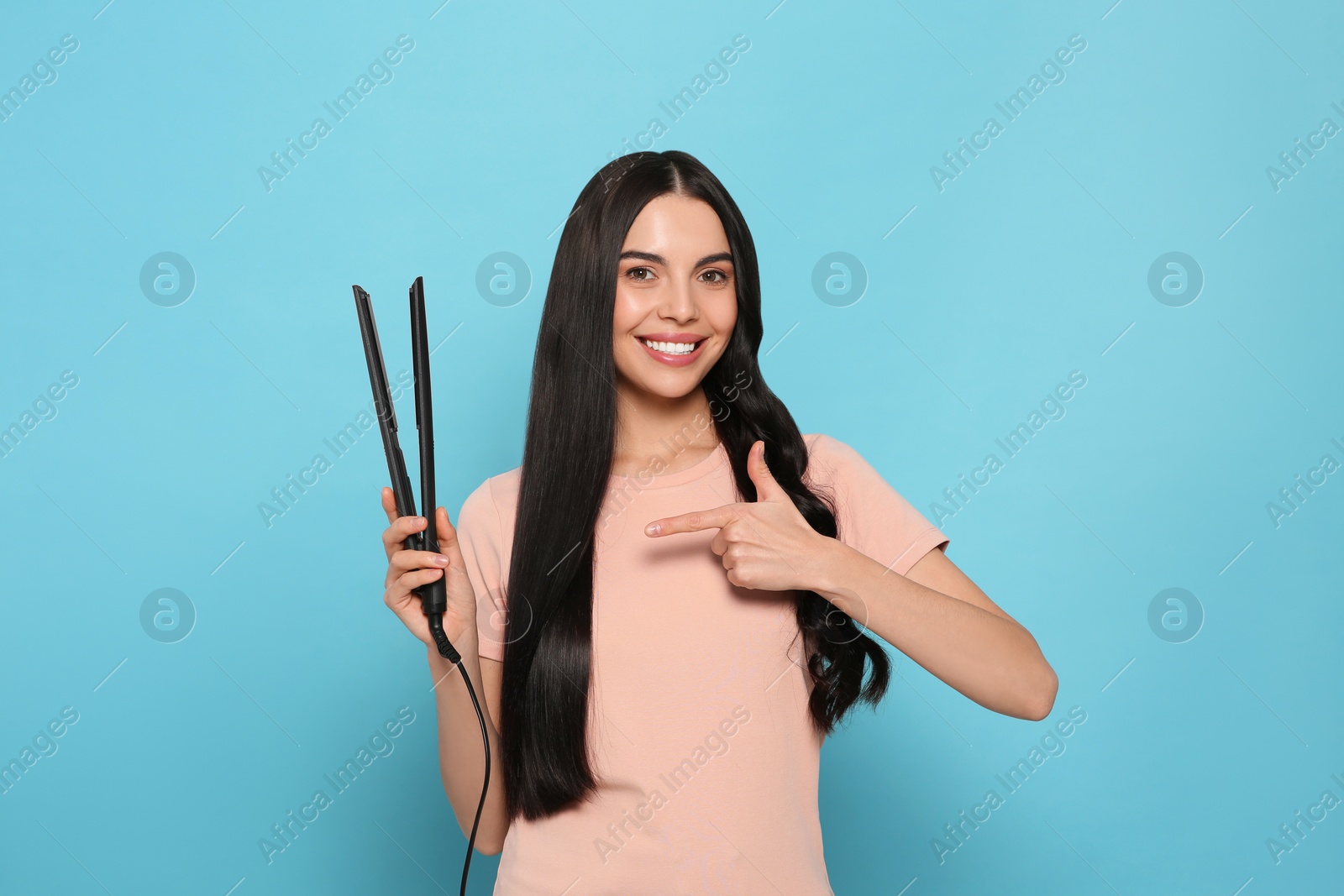 Photo of Beautiful happy woman with hair iron on light blue background