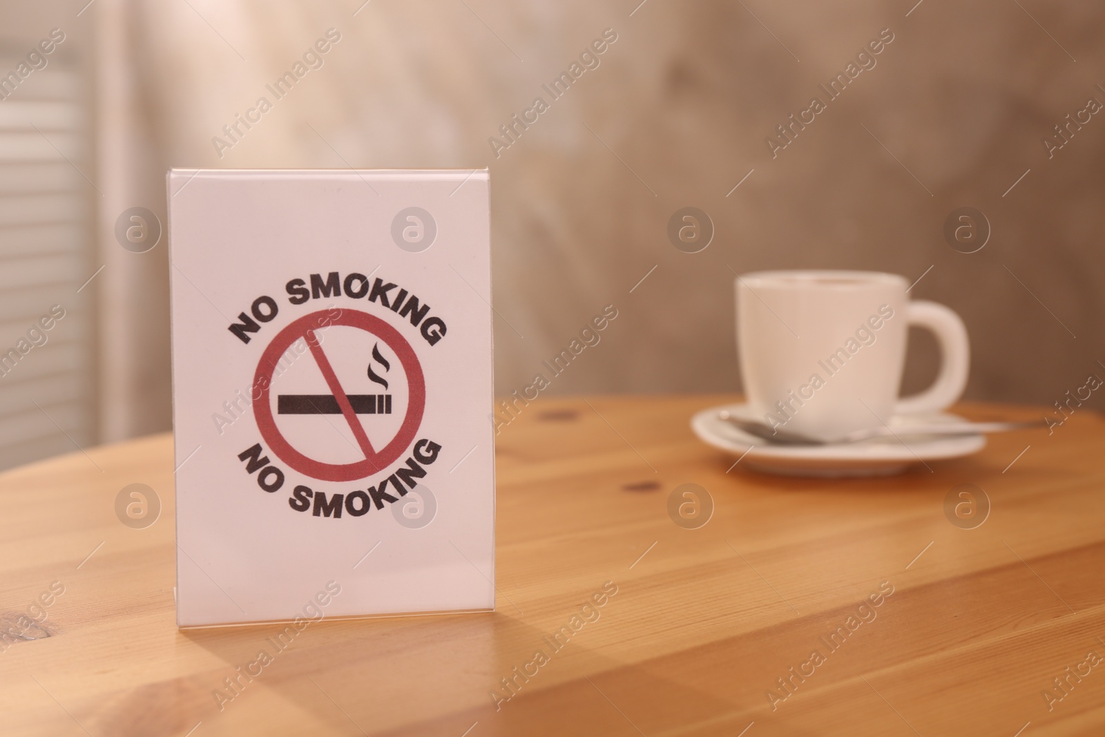 Photo of No Smoking sign and cup of drink on wooden table indoors, selective focus