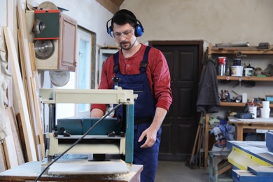 Photo of Mature working man using thickness planer at carpentry shop