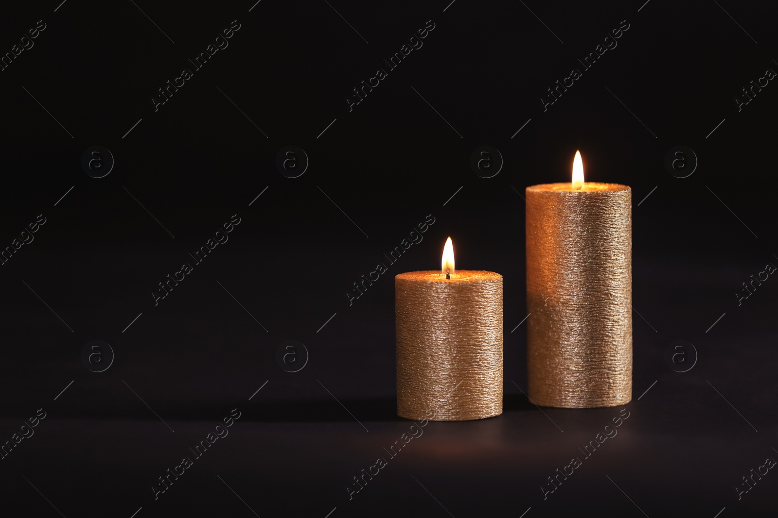 Photo of Burning gold candles on black background, space for text