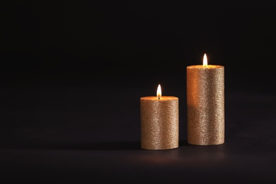 Photo of Burning gold candles on black background, space for text