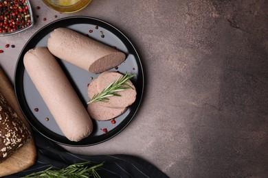 Photo of Delicious liver sausages with rosemary on brown textured table, flat lay. Space for text