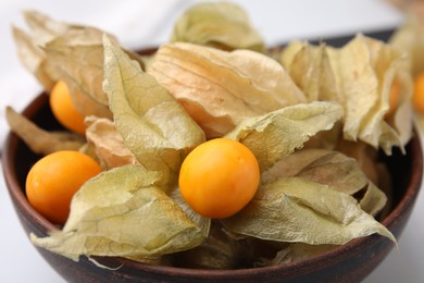 Photo of Ripe physalis fruits with calyxes in bowl on white table, closeup