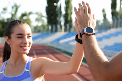 Photo of Couple with fitness trackers giving each other high fives after training at stadium