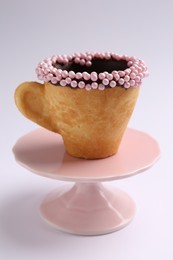 Delicious edible biscuit cup decorated with sprinkles on white background